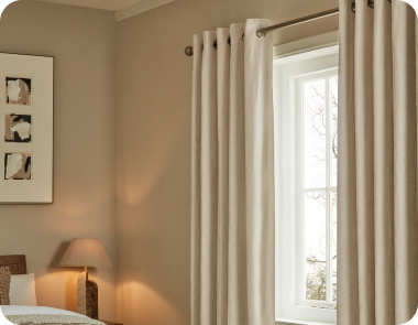 Cream eyelet curtains hang over a window with soft light filtering through.